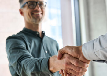 Two smiling professionals engage in a corporate handshake within an office