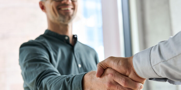 Two smiling professionals engage in a corporate handshake within an office