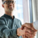 Two smiling professionals engage in a corporate handshake within an office