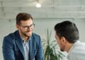 A smiling middle-aged new employee is welcomed to an onboarding meeting with a human resources operative