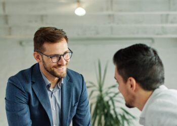 A smiling middle-aged new employee is welcomed to an onboarding meeting with a human resources operative