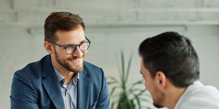 A smiling middle-aged new employee is welcomed to an onboarding meeting with a human resources operative