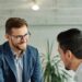 A smiling middle-aged new employee is welcomed to an onboarding meeting with a human resources operative