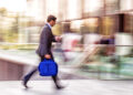 Business professional walking quickly with motion blur while looking at phone, illustrating speed and fast-paced financial activity