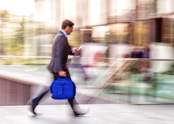 Business professional walking quickly with motion blur while looking at phone, illustrating speed and fast-paced financial activity