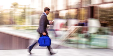 Business professional walking quickly with motion blur while looking at phone, illustrating speed and fast-paced financial activity