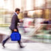 Business professional walking quickly with motion blur while looking at phone, illustrating speed and fast-paced financial activity